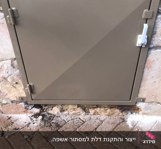 דלת מתכת מרובעת עם ידית לבנה על קיר אבן